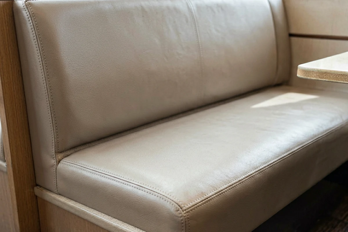 Close-up of a beige vinyl restaurant booth seat and backrest showing detailed stitching and material texture.