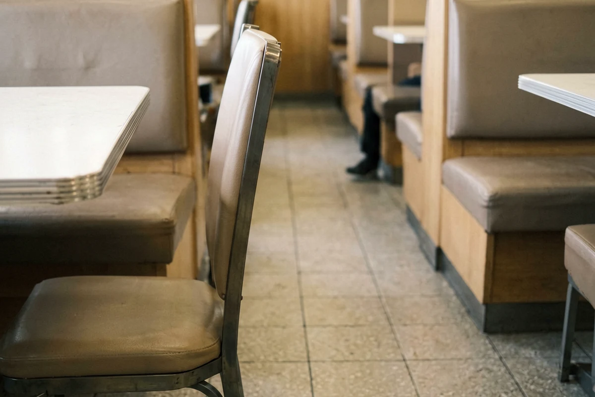 A perspective view of a restaurant dining area showing booth seating on both sides of a central tiled aisle with a standalone chair in the foreground.